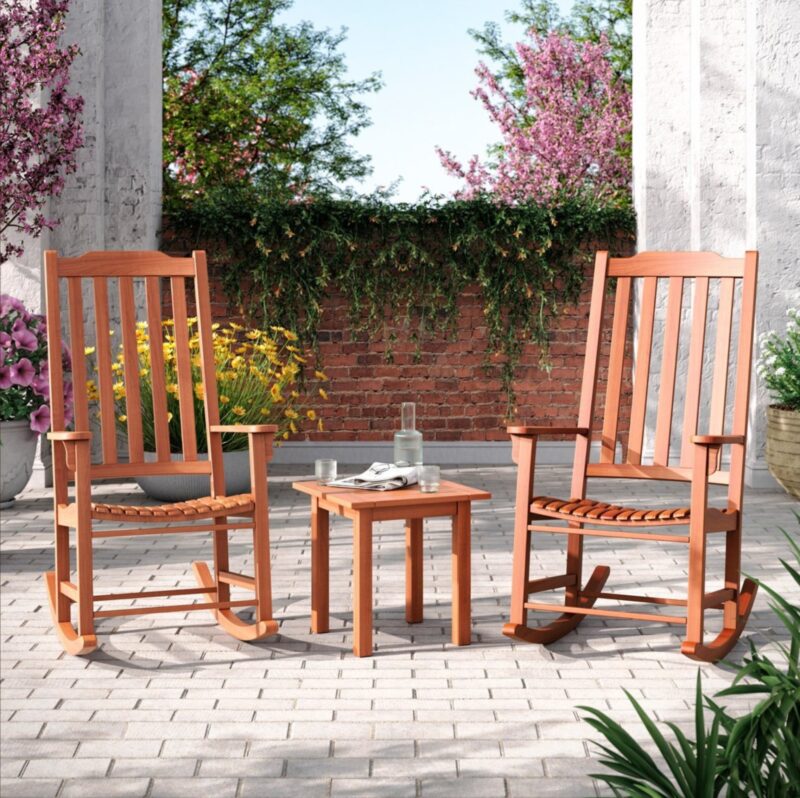 two brown outdoor rocking chairs on a patio and a wooden coffee table with water and glasses on top of the table